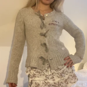 Cardigan - Grå stickad kofta från Odd Molly. Med rosetter framtill och unik design med ”hål” på sidan av ärmarna