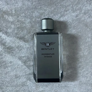 Bentley Momentum Intense - Säljer en elegant Bentley Momentum Intense parfym. Flaskan är stilren och rektangulär med en metallisk grå färg och ett snyggt mönstrat lock. Perfekt för den som vill ha en sofistikerad doft med en touch av lyx. Passar både till vardags och speciella tillfällen. Flaskan är nästan full, så det finns mycket kvar att njuta av!