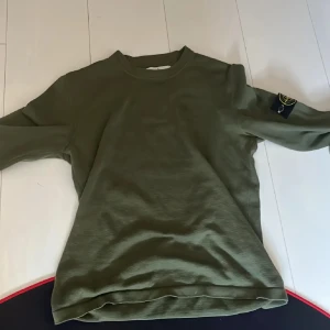 Olivgrön tröja från Stone Island - Säljer en snygg olivgrön tröja från Stone Island. Den har en klassisk design med långärmad passform och det ikoniska Stone Island-märket på ärmen. Perfekt för både vardag och lite mer avslappnade tillfällen. Tröjan är i bra skick och redo för en ny ägare!