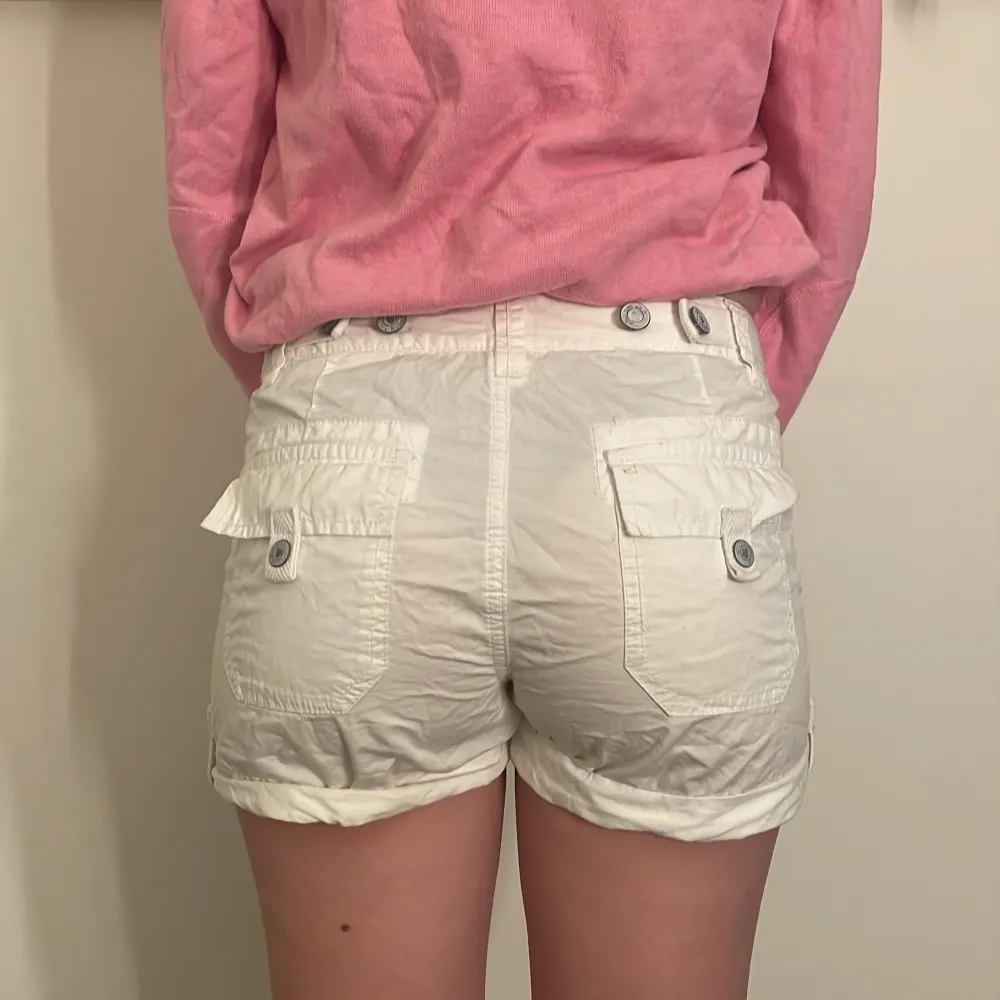 Säljer ett par vita cargo shorts i bomull med knappar framtill och bakfickor med knappdetaljer. De är perfekta för sommaren och har en avslappnad passform. . Shorts.