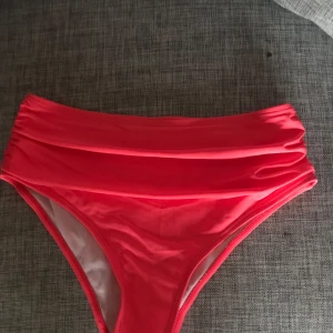 Rosa bikiniunderdel - Säljer en snygg rosa bikiniunderdel i mycket bra skick. Den har en hög midja och är gjord i ett glansigt material som ger en lyxig känsla. Perfekt för sommarens stranddagar eller poolpartyn. Passar bra för både bad och solning. Storleken är inte angiven, men den ser ut att ha en normal passform.