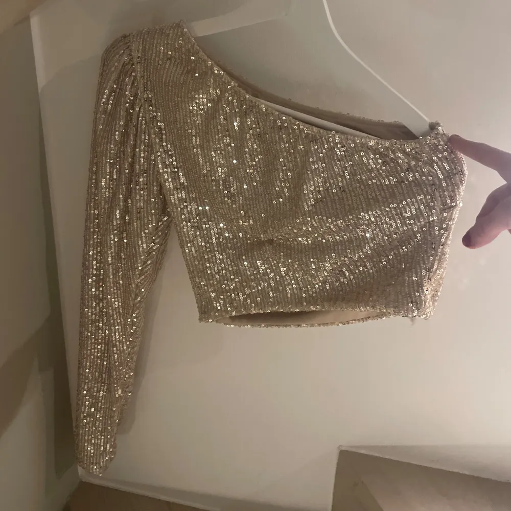 Säljer en superfin glittrig oneshoulder topp i guld. Perfekt för festliga tillfällen! Den är croppad. ✨. Toppar.