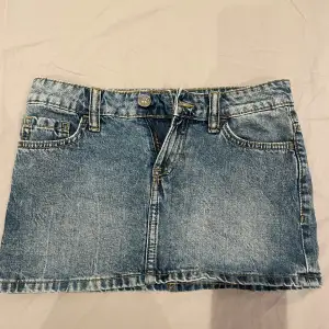 Säljer en snygg mini jeanskjol i blå denim med klassisk femficksdesign. Kjolen har en knapp och dragkedja framtill samt två bakfickor med knappar.💕