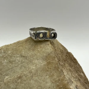 Silverfärgad YOLO-ring - Cool och trendig ring i silverfärg med texten 'YOLO'. Perfekt accessoar för att uttrycka din unika stil och attityd. Passar både till vardags och festliga tillfällen. Ringen har en robust design och är ett måste för alla som älskar att sticka ut.