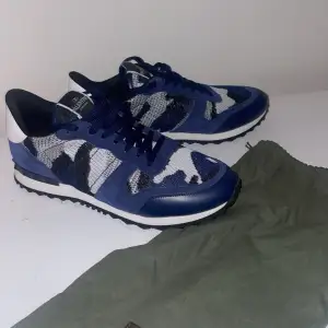 Säljer ett par snygga Valentino Rockrunner sneakers i blått och vitt färg som nästan är omöjliga att få tag i!!.De har ett coolt camouflagemönster och är gjorda i en mix av skinn och textil. Perfekta för att ge din outfit en lyxig touch. Skorna är i mycket bra skick och kommer med originalpåse.