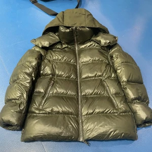 Grön dunjacka från Massimo Dutti - Säljer en snygg grön dunjacka från Massimo Dutti. Jackan har en glansig yta och är perfekt för kalla dagar. Den har en dragkedja framtill och praktiska fickor. Huvan ger extra skydd mot väder och vind. Perfekt för vintern!