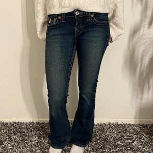 Mörkblå jeans från True Religion - Säljer ett par snygga mörkblå jeans från True Religion i modellen Joey. De har en tight passform med bootcut-stil och är dekorerade med snygga sömmar och knappar på bakfickorna. Perfekta för både vardag och fest! 🕺