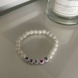 Pärlarmband med bokstäver och hjärta - Säljer ett superfint pärlarmband med vita pärlor och bokstäverna HSLT samt ett rött hjärta. Perfekt för att ge en personlig touch till din stil!