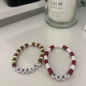 Personliga pärlarmband med namn - Två supergulliga armband med pärlor i olika färger. Det ena armbandet har vita, gröna och vinröda pärlor med bokstäver som bildar namnet 'LORELAI'. Det andra armbandet har vita och vinröda pärlor med bokstäver som bildar namnet 'RORY'. Perfekta som personliga presenter eller för att matcha med en vän!