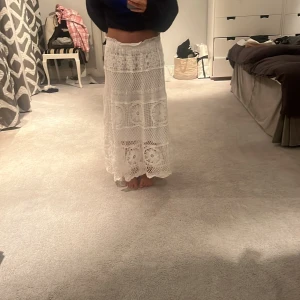 Vit virkad långkjol - Säljer en vacker vit virkad långkjol med detaljerade mönster. Kjolen har en elastisk midja och ett luftigt fall, vilket gör att den inte har någon exakt storlek. Köpt i Spanien i en liten butik