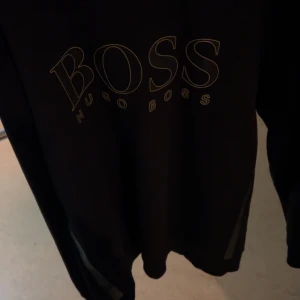 Svart tröja från Hugo Boss - Snygg svart tröja från Hugo Boss med stort tryck på framsidan. Perfekt för en stilren look. Passar bra till både jeans och chinos.