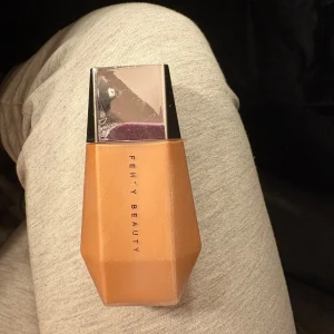 Fenty Beauty Eaze Drop Lit All-Over Glow Enhancer - Oanvänd Fenty Beauty Eaze Drop Lit All-Over Glow Enhancer i nyansen Honey Citrine. Denna produkt ger en strålande glow och kommer i en elegant, geometrisk flaska med silverlock. Innehåller 36 ml.