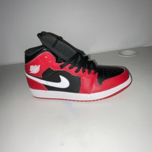 Nike Air Jordans i svart och rött - Snygga Nike Air Jordans i klassisk svart och röd färgkombination med vit sula. Skorna har en ikonisk design med snörning och det välkända Nike-logotypen på sidan. Perfekta för dig som vill ha en stilren och sportig look.