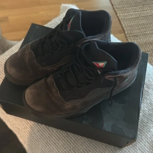 Jordan Max Aura 2 i brun och svart - Snygga Jordan Max Aura 2 sneakers i en kombination av brun mocka och svart syntetmaterial. Skorna har en stilren design med snörning och detaljer i neptungrön. Perfekta för dig som vill ha en sportig och trendig look.