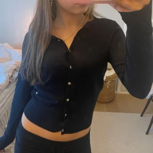 Svart kofta med knappar - Snygg svart kofta med knappar framtill. Perfekt för en stilren look och enkel att matcha med olika outfits. Långärmad design som ger en klassisk touch.