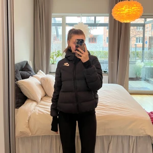 Svart dunjacka - Snygg och trendig pufferjacka från Nike i svart och vitt. Jackan har en normal passform och är perfekt för kyligare dagar. Den har en dragkedja framtill och en hög krage för extra värme. Perfekt för att hålla stilen i vinter! Denna är vändbar och blir sol två jackor i en :) Står ingen storlek pga vändbar men skulle tippa på 34/36. Jag är 165cm lång och vanligtvis en S.