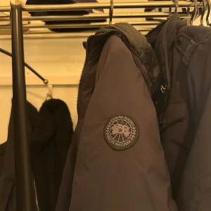 Svart dunjacka från Canada Goose - Säljer min Canada Goose Lodge Hoody Black Lable. Storlek S. Det är i väldigt bra skick utöver att det är ett hål som är mindre än ett riskorn som man kan se bredvid mitt finger på sista bilden. Jackan är köpt på careofcarl där nypris är 9 599kr. Inga fläckar eller tecken på användning då jag bara haft den förra vintern och ej använt denna vintern. Jackan är gjort för 0 till -15 grader. 