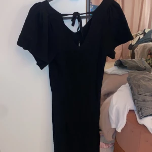 Svart klänning  - Snygg svart klänning med korta ärmar och v-ringning. Den har ett knytband i ryggen som ger en fin detalj. Använd bara en gång eftersom att den var lite för liten. 