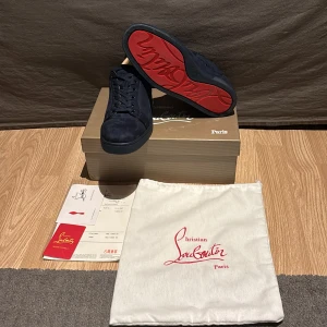 Svarta sneakers från Christian Louboutin - Snygga svarta sneakers från Christian Louboutin med den ikoniska röda sulan. Skorna är tillverkade i mocka och har en stilren design med snörning. Perfekta för den som vill ha en touch av lyx i vardagen.