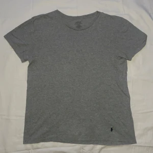 Grå t-shirt från Polo Ralph Lauren - Säljer en klassisk grå t-shirt från Polo Ralph Lauren i 100% bomull. T-shirten har en broderad logga i mörkblått i hörnet och är kortärmad med en normal passform. Perfekt för en avslappnad stil.