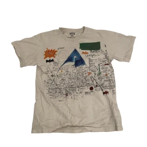 Vit Uniqlo t-shirt - Säljer en cool vit t-shirt från Uniqlo med ett unikt grafiskt tryck i flera färger. Perfekt för dig som gillar att sticka ut med din stil. T-shirten har korta ärmar och är gjord i mjukt bomullsmaterial. 