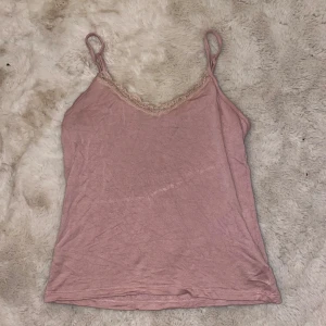 Rosa linne med spetsdetalj - Säljer ett sött rosa linne med smala axelband och spetsdetalj vid halsringningen. 