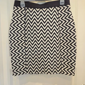 Svartvit kjol med zigzag-mönster - Snygg svartvit kjol med ett iögonfallande zigzag-mönster. Kjolen har en dragkedja baktill och är tillverkad i en blandning av polyester och viskos för en bekväm passform. Perfekt för att ge din outfit en trendig touch!