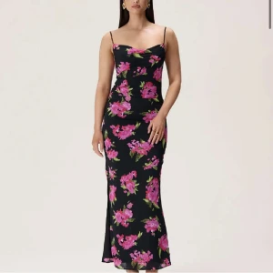 Svart blommig långklänning från ADOORE - Snygg svart långklänning från ADOORE med rosa blommönster. Klänningen har smala axelband och en knytning bak. STORLEK 38