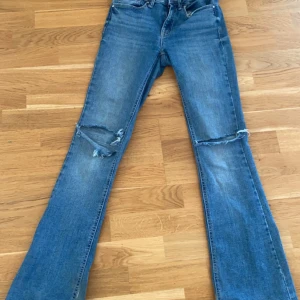Blå bootcut jeans från Vero Moda - Snygga blå bootcut jeans från Vero Moda med slitna detaljer på knäna. De har en klassisk femficksdesign och är tillverkade i jeansmaterial. Perfekta för en avslappnad stil.
