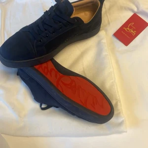 Mörk blå sneakers  från Christian Louboutin - Snygga mörkblå  sneakers från Christian Louboutin med den ikoniska röda sulan. Skorna har en stilren design med snörning och är tillverkade i ett elegant material. Perfekta för den som vill ha en touch av lyx i vardagen. Priset är inte hugget i sten 🪨 med en liten skråma på
