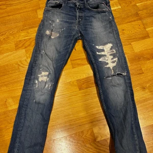 Blå jeans från Replay - Snygga blå jeansbyxor från Replay med slitna detaljer och en cool look. Modellen är Grover och har en klassisk femficksdesign. Perfekta för en avslappnad stil.