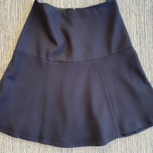 Marinblå kjol från Filippa K - Elegant marinblå kjol från Filippa K i en klassisk design. Kjolen har en dragkedja i sidan och är tillverkad i en blandning av polyester och viskos för en bekväm passform. Perfekt för en stilren look. Ny marinblå kjol i strl XS från Filippa K.  Kjolen har en underkjol  Ny, aldrig använd.  Mått Midjan: ca 36 cm Total längd: ca 49 cm  67% polyester, 29% viskos och 4% elastan  Kommer från ett djur och rökfritt hem. 