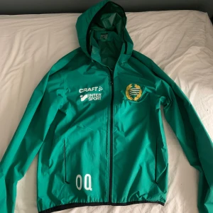 Hammarby vindjacka - Säljer en grön hammarby-vindjacka från Craft med huva och dragkedja då jag växt ur den. Något använd men i så gott som nytt skick. Initialer kan filas bort!