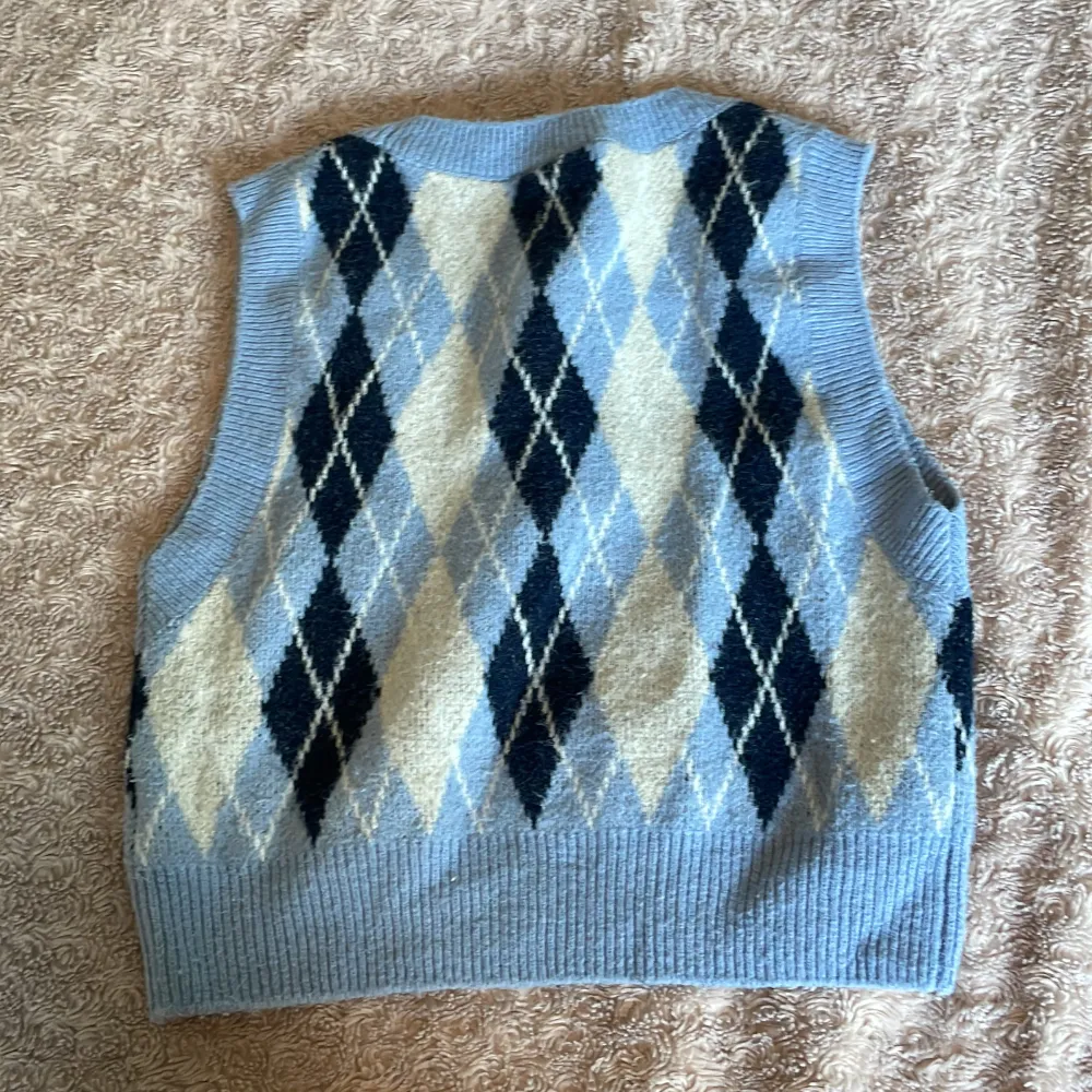 Säljer en snygg ljusblå stickad väst från Monki med ett klassiskt argylemönster i mörkblått och vitt. Perfekt för lager-på-lager-stil och ger en retro touch till din outfit. 🧶✨. Yläosat.