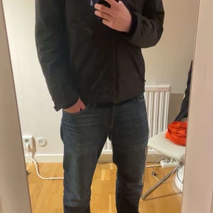 Svart jacka från Sail Racing - Snygg svart jacka från Sail Racing med dragkedja och huva. Perfekt för kyligare dagar. Jackan har en stilren design med en bröstficka och diskreta logodetaljer. Skick 9/10