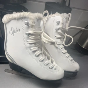 Vita konståkningsskridskor  - Säljer ett par vita konståkningsskridskor från Spin med snörning och mjuk pälsdetalj runt skaftet. Skridskorna har en klassisk design med robusta blad för bra glid på isen. Lita skråmor där framme vid tårna men inget rost på bladet. Storlek 34