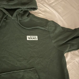 Grön hoodie från Vans - Säljer en snygg grön hoodie från Vans med klassisk logga på bröstet. Perfekt för en avslappnad stil. Den har en justerbar huva och långa ärmar. Passar perfekt till vardags eller för en skön dag ute.