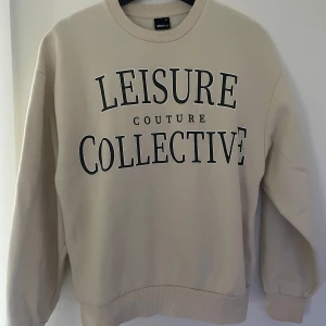 Beige sweatshirt från Gina Tricot - Säljer en beige sweatshirt från Gina Tricot med texten 'Leisure Collective' tryckt på framsidan. Tröjan har långa ärmar och en rund halsringning med ribbade muddar vid ärmslut och nederkant. I storlek Xs men sitter jätte bra på en med S också då den är lite oversize. Använd någon enstaka gång så i väldigt bra skick!