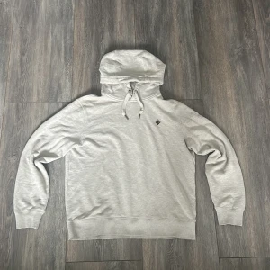 Beige hoodie från Morris - Snygg beige hoodie från Morris med en liten broderad detalj på bröstet. Tröjan har en justerbar huva med snören och ribbade muddar vid ärmslut och nederkant. Perfekt för en avslappnad stil. Storlek S. Priset är inte hugget i sten. Skriv privat för frågor!