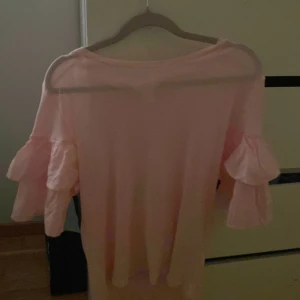 Rosa tröja med volangärmar - Säljer en söt rosa tröja med volangärmar. Perfekt för en feminin och stilren look. Tröjan har en rund hals och är tillverkad i ett mjukt material.