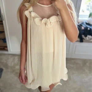 Creamvit volang klänning - Säljer en söt beige ärmlös klänning med volangdetaljer och transparent övre del. 