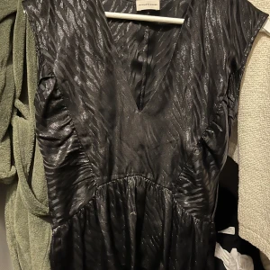 By Malene Birger topp - Snygg svart topp från By Malene Birger med ett glittrigt mönster. Klänningen har en v-ringad design och är ärmlös, vilket ger en elegant look. Perfekt för speciella tillfällen eller en utekväll.