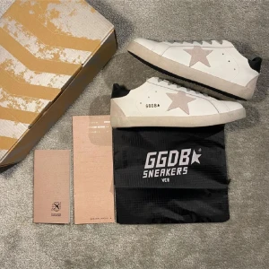  Golden Goose skor - Snygga vita sneakers från Golden Goose med en stjärndetalj på sidan. Skorna har en svart häl med märkeslogga och en vit sula med svart undersida. Perfekta för en stilren look.