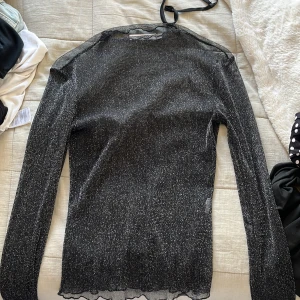 Svart glittrig topp från NA-KD - Säljer en svart glittrig topp från NA-KD i storlek XS. Toppen är långärmad och aldrig använd 