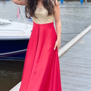 Röd och guldklänning - Elegant långklänning med en glittrig guldöverdel och röd kjol. Klänningen har en v-ringad design och är ärmlös, vilket ger en stilren och festlig look. Perfekt för speciella tillfällen. Som bal, klänningen är coustum maid så finns ej att köpa i butik, den är i silkes material och dubbel tyg inne så de ej sticks av glitter tyget (pris kan diskuteras) fler bilder finns privat 