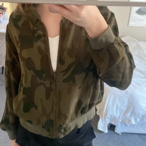 Camouflage bomberjacka - Säljer en cool bomberjacka i camouflage-mönster. Jackan har dragkedja framtill och långa ärmar med ribbade muddar. Perfekt för en avslappnad och trendig look. Har vissa fläckar men ingeting man märker av !! 