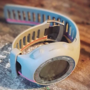 Blå sportklocka från Garmin - Säljer en blå sportklocka från Garmin med en rund urtavla och flera funktionella knappar runt kanten. Armbandet är justerbart med rosa detaljer och har en robust design, perfekt för träning.