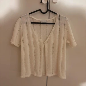 Vit stickad kofta - Säljer en söt vit stickad kofta med korta ärmar och v-ringning. Koftan har ett diskret randigt mönster och en knapp framtill. Perfekt för lager-på-lager-stil eller sommarens svalare kvällar.