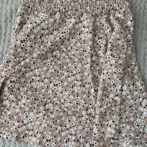 Beige blommig kjol från 157 - Söt beige kjol med blommigt mönster från 157. Kjolen har en elastisk midja för bekväm passform och är perfekt för en avslappnad stil. Den är kort och har ett lätt och luftigt material.