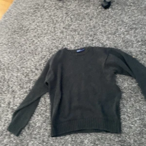 Mörkgrå stickad tröja från Ralph Lauren - Säljer en stilren mörkgrå stickad tröja från Ralph Lauren. Tröjan har en klassisk rund hals och långa ärmar, perfekt för kyligare dagar. Den är i storlek L och passar bra till både jeans och chinos. Ett måste i garderoben för den som gillar tidlös design.